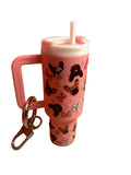 Pink tumbler with dog designs and a straw, attached to a keychain, on a beige surface.