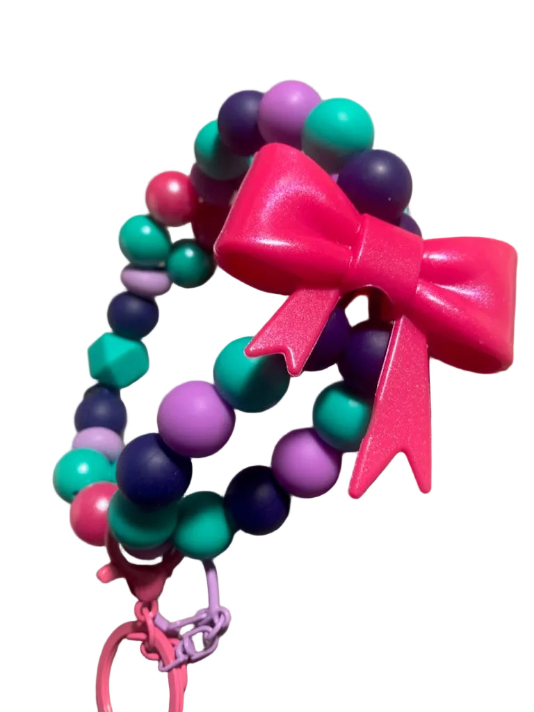 Colorful beaded bracelet with a pink bow and keychain on a beige surface